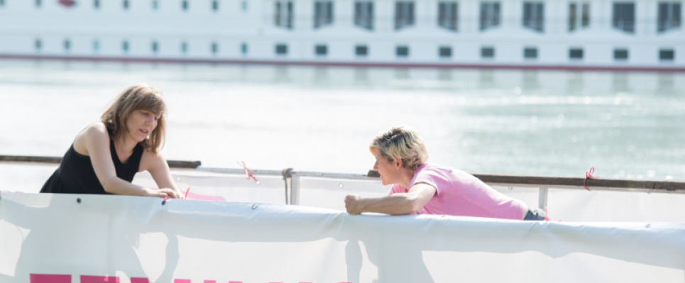 Zwei Personen befestigen ein Banner mit der Aufschrift "FEMINISTISCH" an einem Geländer.