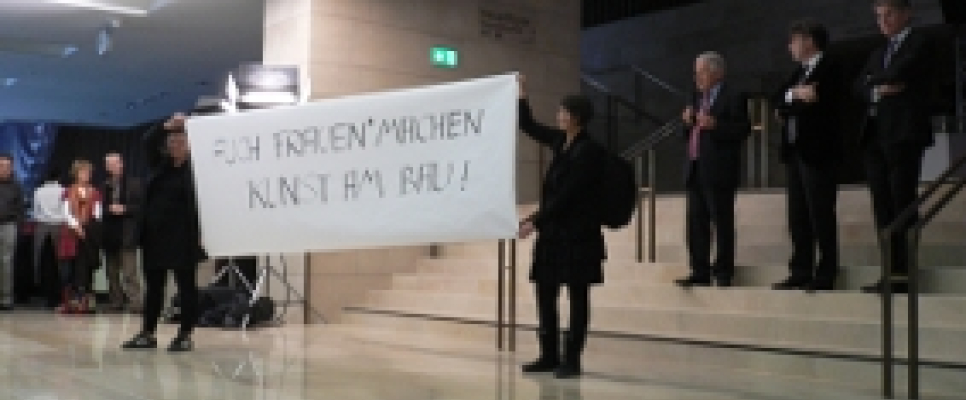 Personen mit Transparent in modernem Gebäude, Publikum im Hintergrund.