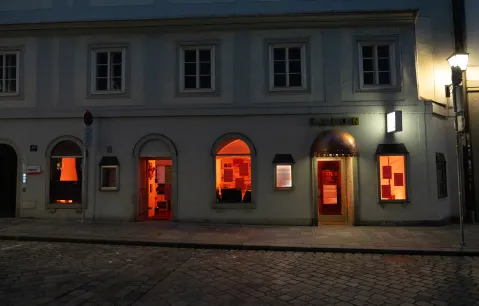 Eingang eines Gebäudes bei Nacht, Fenster leuchten orange.
