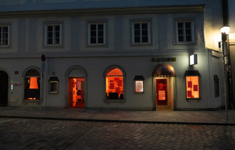 Eingang eines Gebäudes bei Nacht, Fenster leuchten orange.