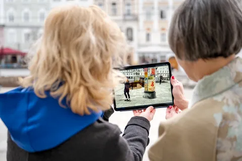 Zwei Frauen betrachten ein Foto auf einem Tablet im Freien.