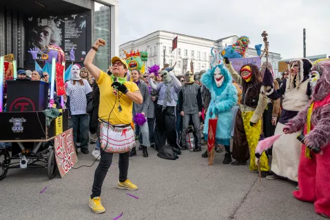 Demonstration mit verkleideten Menschen, bunte Kostüme, führende Person in gelb.