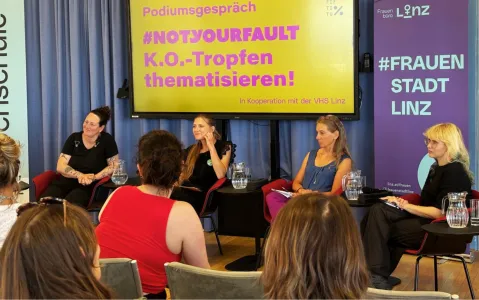 Podiumsdiskussion über K.O.-Tropfen in Linz, vier Frauen sprechen vor gelbem Banner.