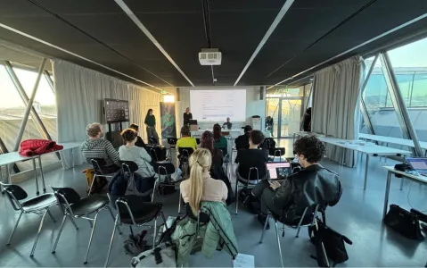 Menschen in Seminarraum, Präsentation vor Projektor, Tageslicht durch Fenster.