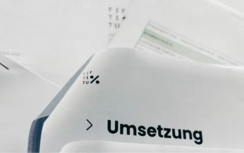 Dokument mit dem Wort "Umsetzung" und einem Logo, verschwommene Hintergrundtexte.