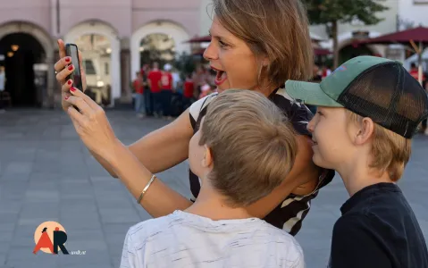 Frau mit zwei Kindern, fasziniert vom Smartphone auf belebtem Platz.