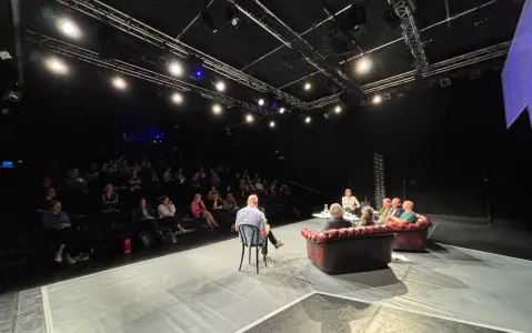 Podiumsdiskussion auf Bühne, Publikum im Dunkeln.