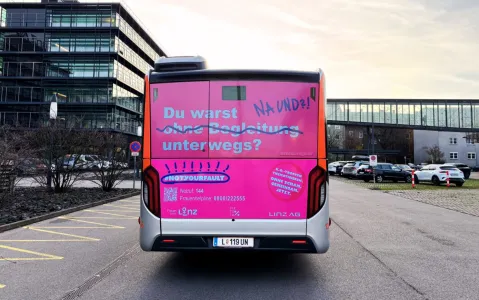 Rosa Bus mit feministischer Botschaft auf einer Straße vor Bürogebäuden.
