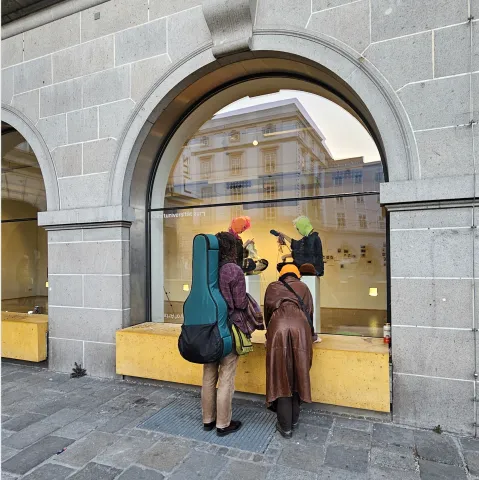 Drei Personen mit farbigen Mützen betrachten eine Schaufensterauslage.