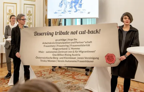Zwei Personen halten ein Plakat mit Organisationen in einem festlichen Raum.