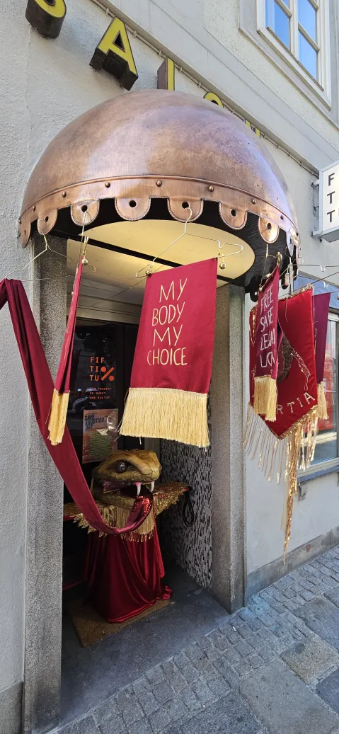 Rote Banner mit Goldrand und Text "MY BODY, MY CHOICE" an einem Eingang.