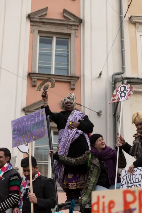 Demonstrant*innen halten Protestschilder vor einem Gebäude während einer Feminist*innen-Demo.