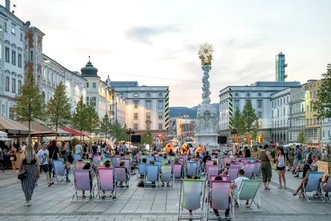 Menschenmenge auf Stadtplatz mit bunter Bestuhlung, Livemusik im Hintergrund.