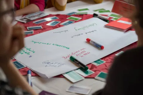 Workshopteilnehmer beschriften Papier auf Tisch mit farbigen Karten und Stiften.