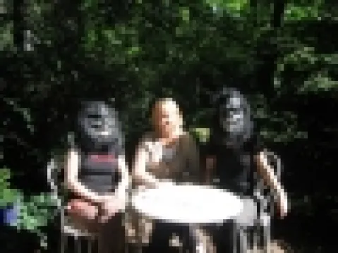 Drei Personen an einem Tisch im Freien, zwei tragen Gorilla-Masken.