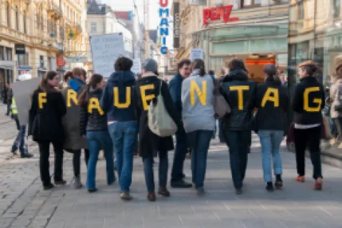 Menschen tragen Buchstaben auf Rücken, die "Frauentag" bilden. Straßenszene.