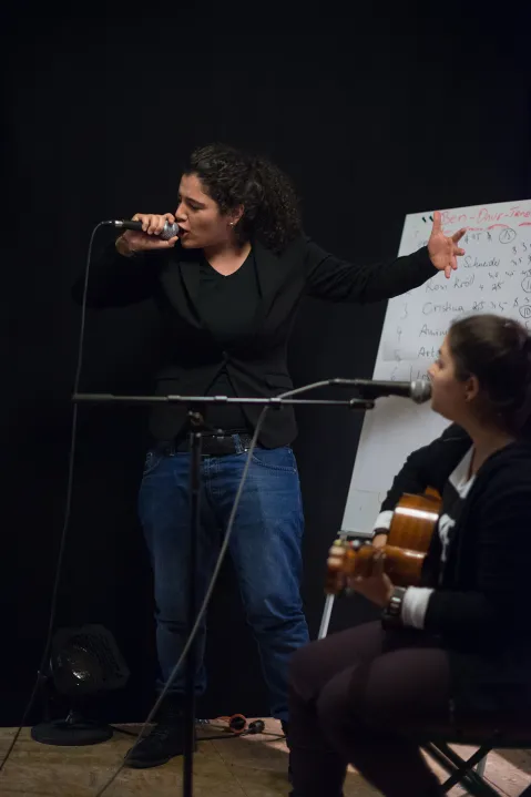 Zwei Personen bei einer Musikprobe, eine singt, die andere spielt Gitarre.