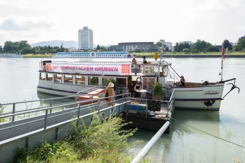 Touristenboot am Ufer eines Flusses, Menschen steigen ein.