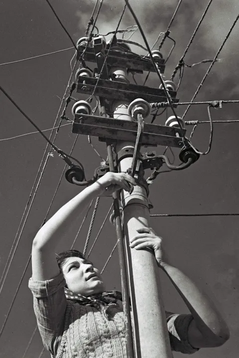 Frau klettert auf Strommast und überprüft Leitungen. Schwarz-weiß Fotografie.