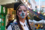 Person in Tracht mit bunter Gesichtsbemalung vor festlicher Kulisse.