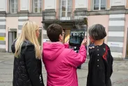 Drei Frauen, eine hält ein Tablet, stehen vor einem historischen Gebäude.