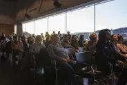 Publikum sitzt aufmerksam bei Tageslicht in einem modernen Konferenzraum.