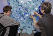 Zwei Personen untersuchen zahlreiche blaue Umschläge auf dem Boden.