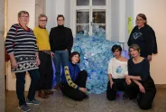 Frauen vor einer Installation aus blauen Plastikflaschen, posieren lächelnd in Galerie.