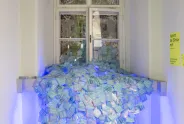 Blaue Lichtinstallation mit Pappkartons vor einem Fenster in einem Flur.