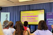 Podiumsgespräch mit Publikum, Thema: K.O.-Tropfen, gelber Bildschirm, blaue Vorhänge.