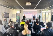 Vortrag in modernem Konferenzraum mit Publikum und drei Präsentierenden.