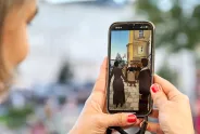 Frau hält Smartphone, zeigt Bild von Frauen beim Protest in der Stadt.