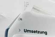 Dokument mit dem Wort "Umsetzung" und einem Logo, verschwommene Hintergrundtexte.