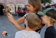 Frau mit zwei Kindern, fasziniert vom Smartphone auf belebtem Platz.