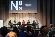 Podiumsdiskussion mit sieben Personen, Logo „Nb“ im Hintergrund.