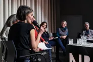 Podiumsdiskussion mit sechs Frauen, eine spricht ins Mikrofon.