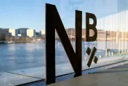 Logo „N×B“ auf Glaswand mit Fluss und Stadt im Hintergrund.