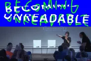 Bühne mit Vortrag, blauer Hintergrund, Publikum, Schriftzug "Becoming Unreadable".