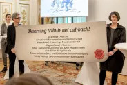 Zwei Personen halten ein Plakat mit Organisationen in einem festlichen Raum.