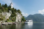 Kirche auf steilem Hügel am See, Boot im Wasser, sonniges Wetter.
