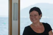 Frau lächelnd vor See und Berg im Hintergrund.