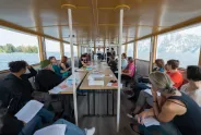 Frauen diskutieren in einer Bootskabine, Seeblick im Hintergrund.