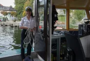 Frau in Kapitänsuniform mit Seil auf einem Boot, lächelnd.