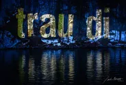 Leuchtende Buchstaben "trau di" über einem Gewässer bei Nacht.