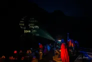 Projektor strahlt feministische Begriffe in der Nacht, umgeben von Zuschauer:innen in Mänteln.