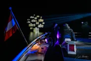 Boot bei Nacht mit Lichtprojektion "alles für alle", Menschen an Deck, österreichische Flagge.