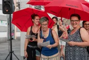 Frauen mit roten Regenschirmen lächeln und lesen in einer Stadt, sommerliche Kleidung.