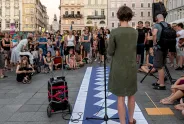Frau hält Rede vor Publikum auf einem Platz, blaue Bahn mit Dokumenten am Boden.