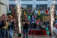 Eine Frau mit Mikrofon vor Bühne mit Band und bunten Lichtern, umgeben von Feiernden.