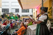 Frau spricht bei Veranstaltung im Hof, buntes Publikum, festliche Dekoration.